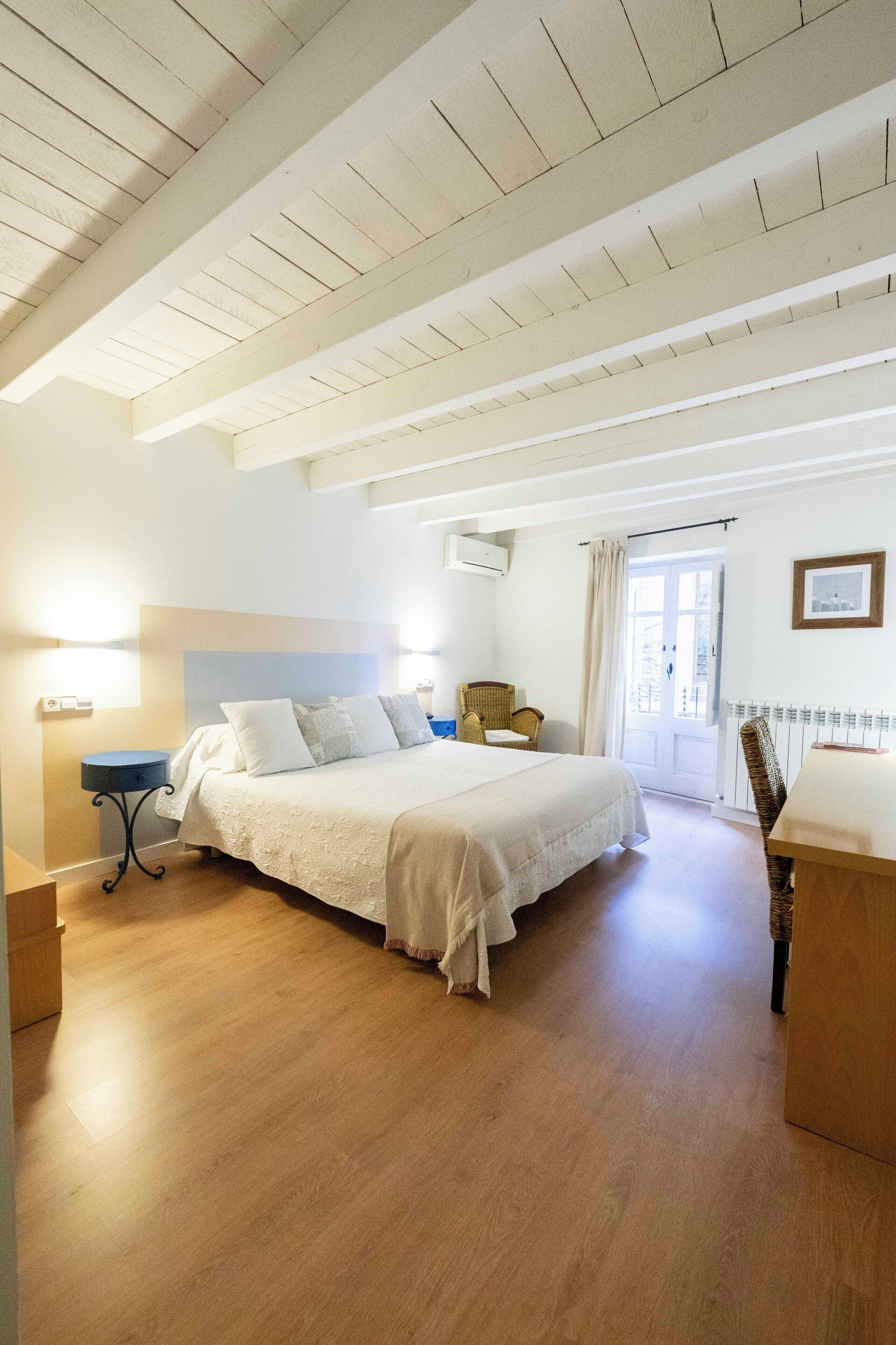 Un dormitorio con una cama grande, una silla, una mesita y una puerta que da a un balcón.