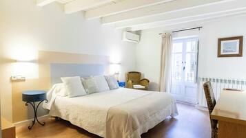 Un dormitorio con una cama grande, una silla, una mesita y una puerta que da a un balcón.