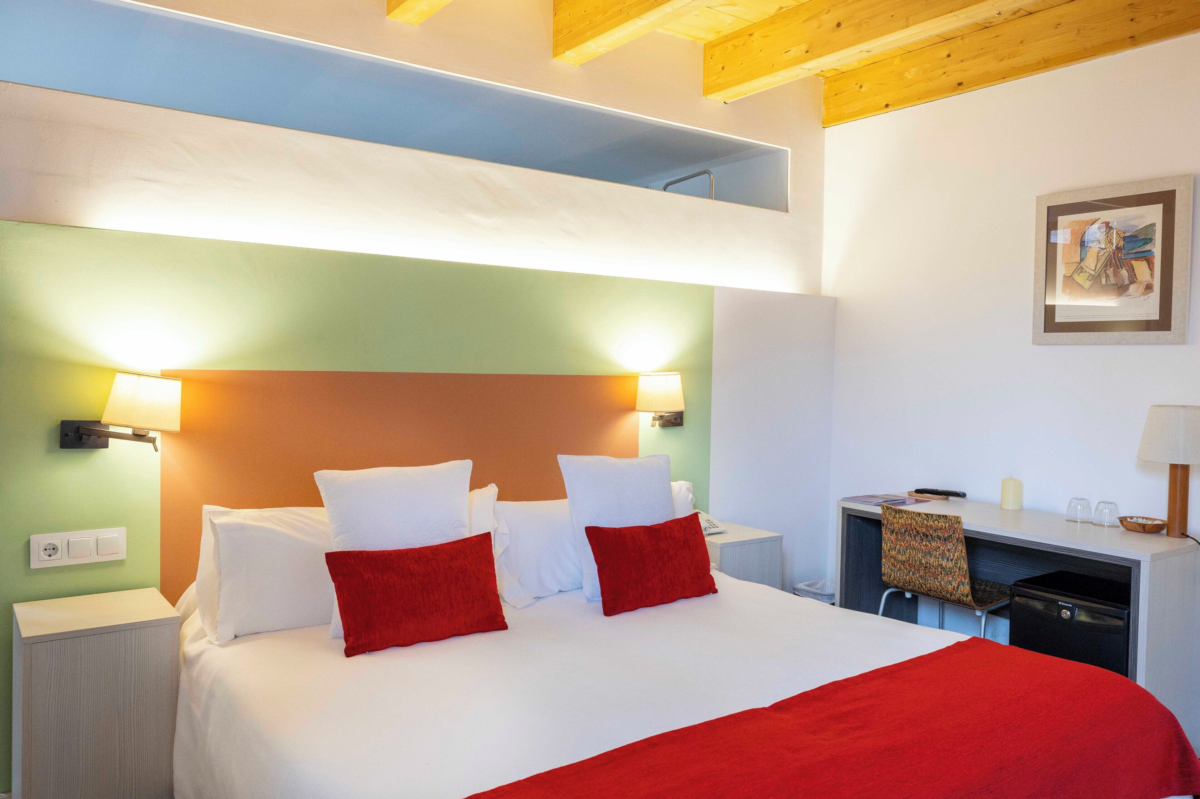 A hotel room with a bunk bed, a desk with a chair, and a small table with a lamp.