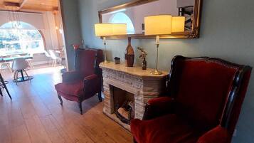 A room with a fireplace, two red armchairs, a large mirror, and a dining area with natural light.