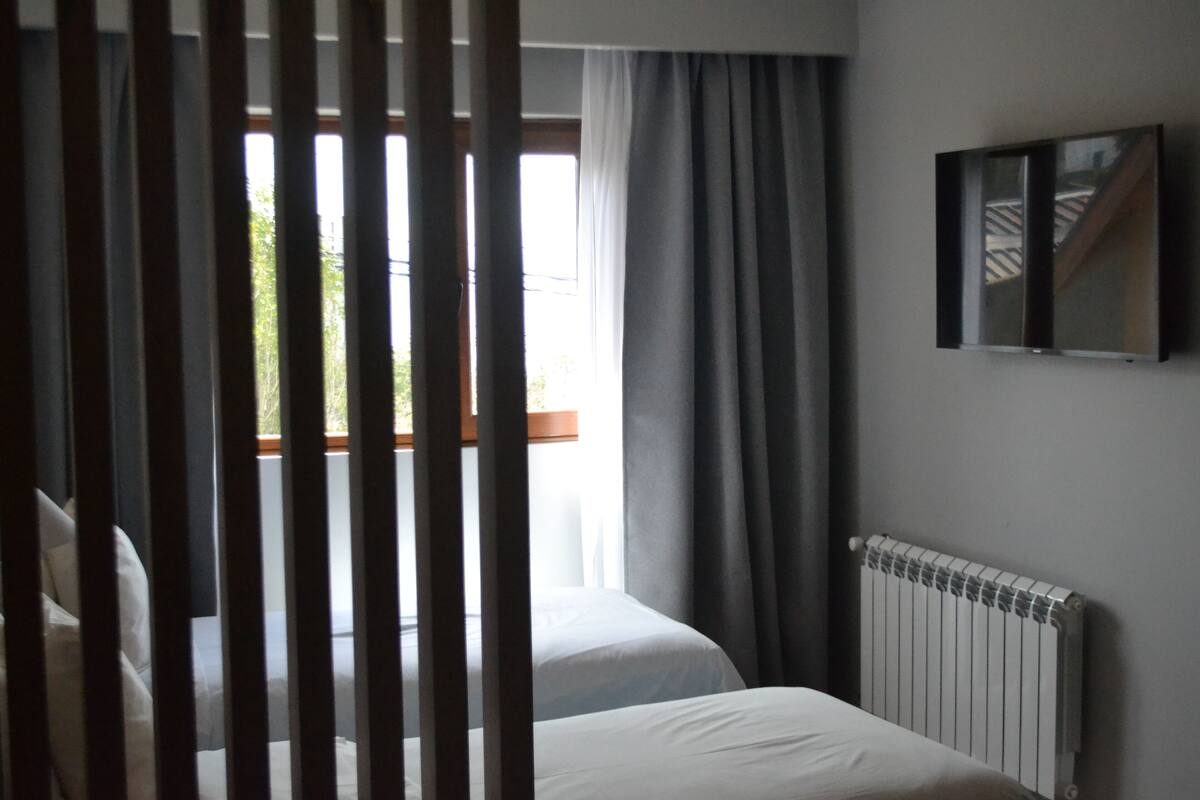Una habitación de hotel con dos camas, una ventana con cortinas, un radiador y un cuadro en la pared.