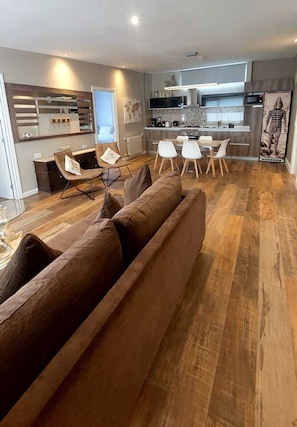 Un salon moderne comprenant un canapĂ©, un coin repas, une cuisine et une grande fenĂȘtre.