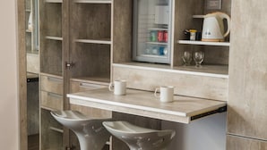 A compact kitchenette with a built-in refrigerator, a coffee maker, and two bar stools. -  Hostería y Restaurante América (Ushuaia)