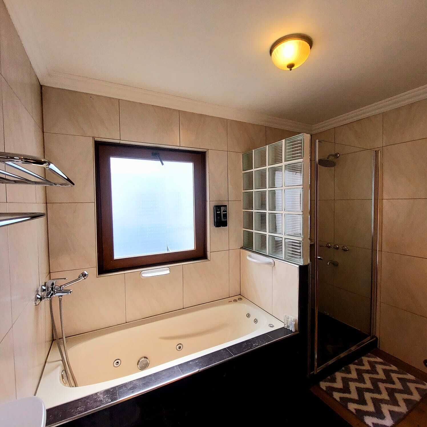 Casa de banho com banheira, chuveiro, armário envidraçado e janela.