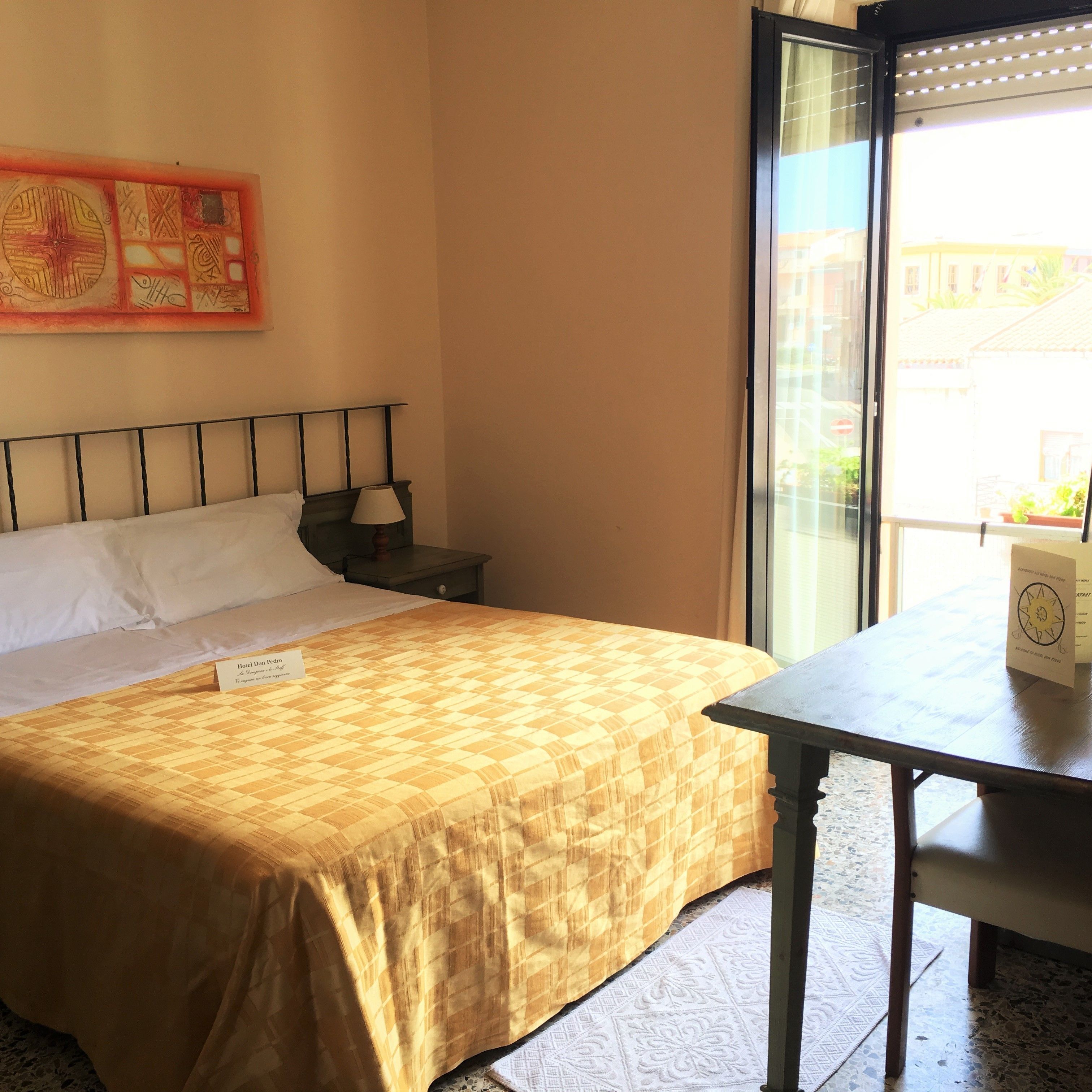 A hotel room with a bed, a nightstand, a table, and a window with a view of the outside.