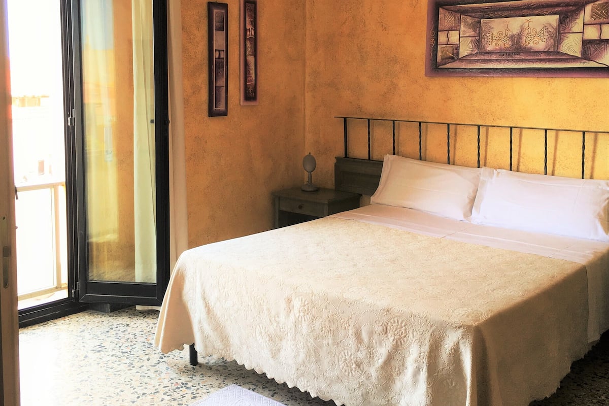 A bedroom with a bed, a nightstand, a painting, and a door leading to an outdoor area.