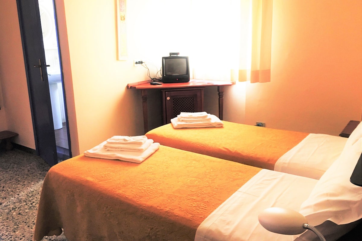 A hotel room with two beds, a television on a wooden table, and a window with curtains.