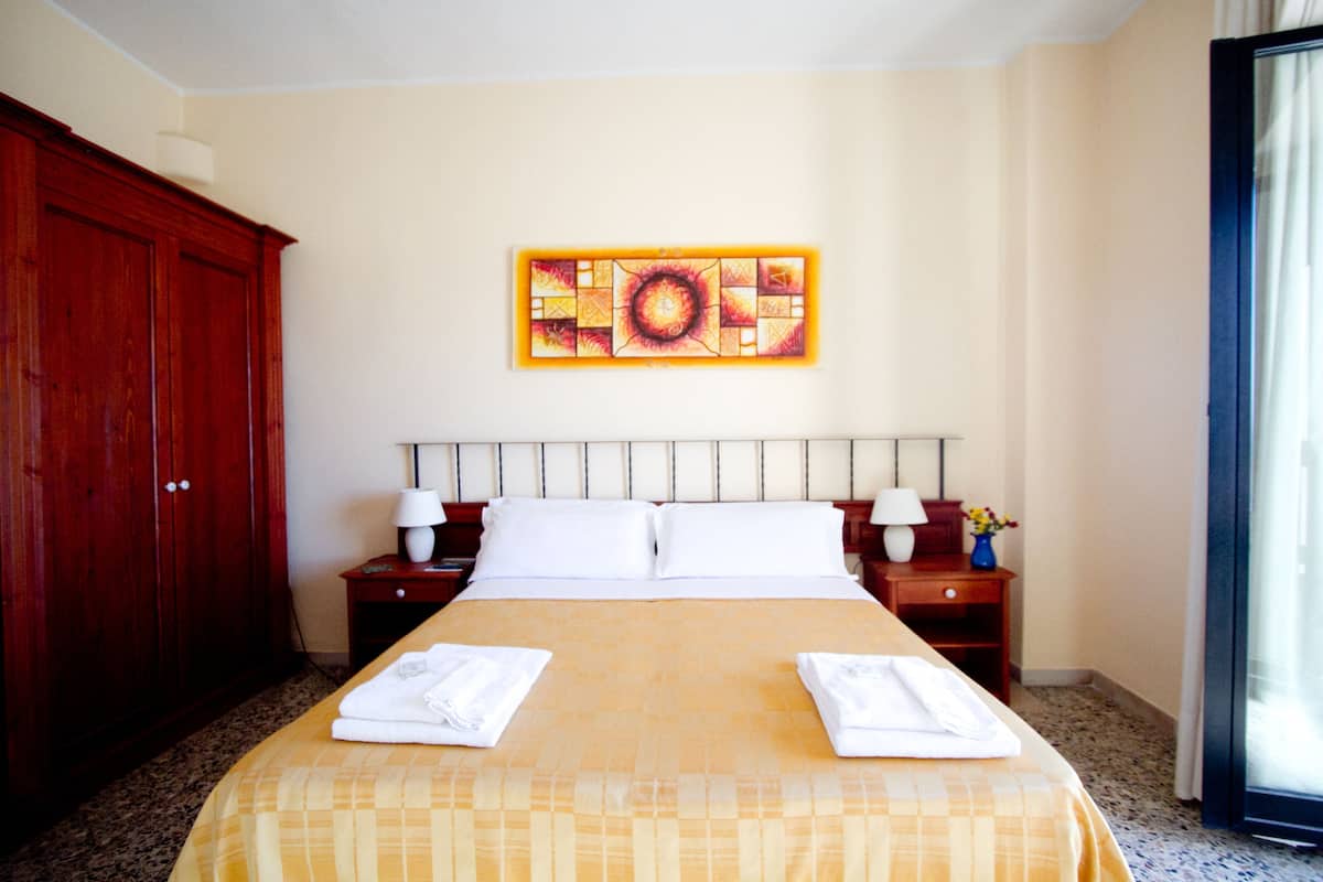 A hotel room with a large bed, two bedside tables with lamps, a wooden wardrobe, and a painting on the wall.
