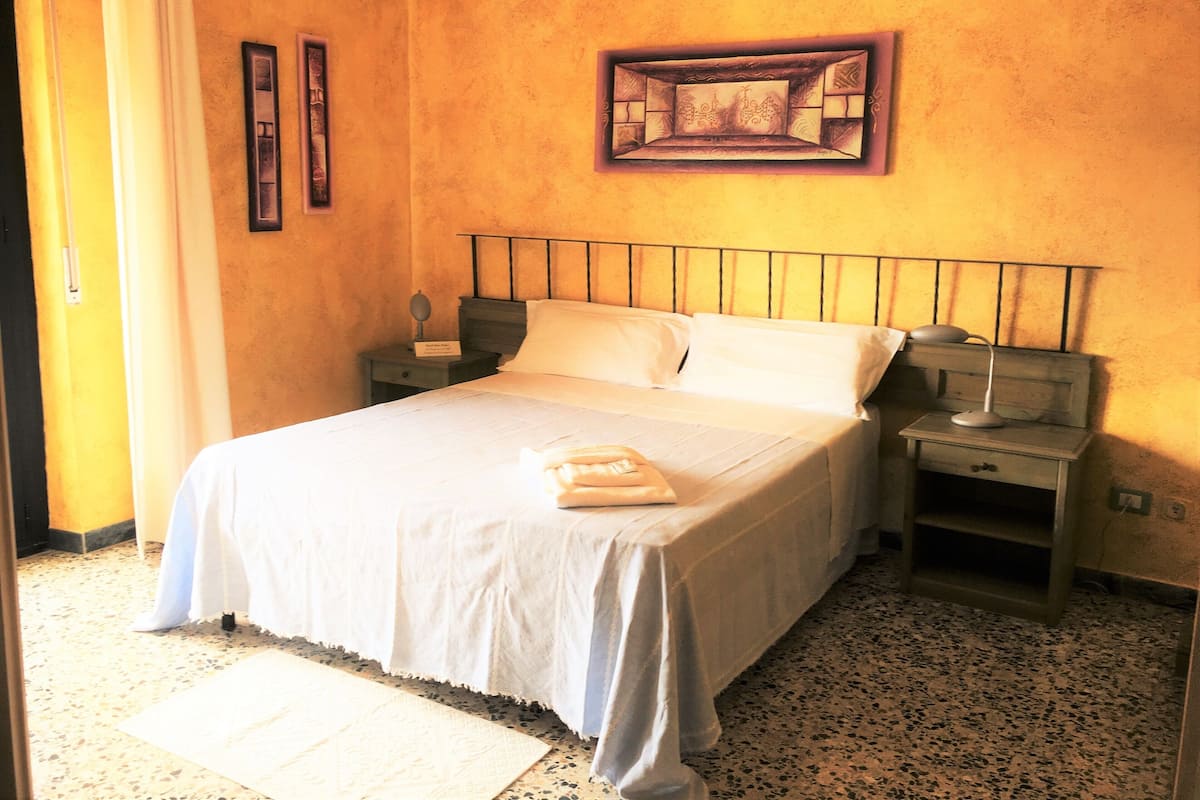 A neatly made bed with white linens, a bedside table with a lamp, and a framed picture on the wall.