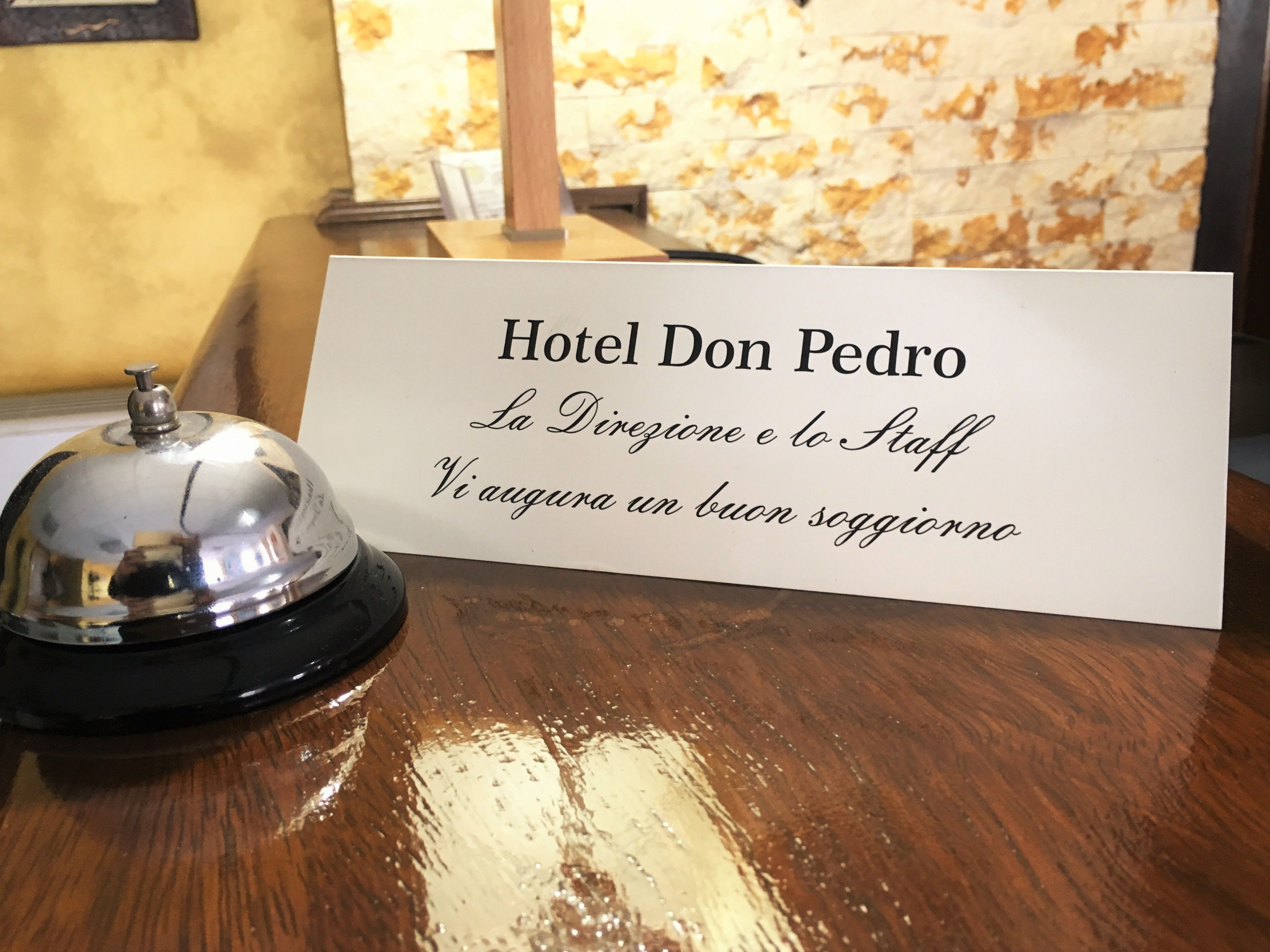 A hotel reception desk with a sign reading "Hotel Don Pedro" and a bell.
