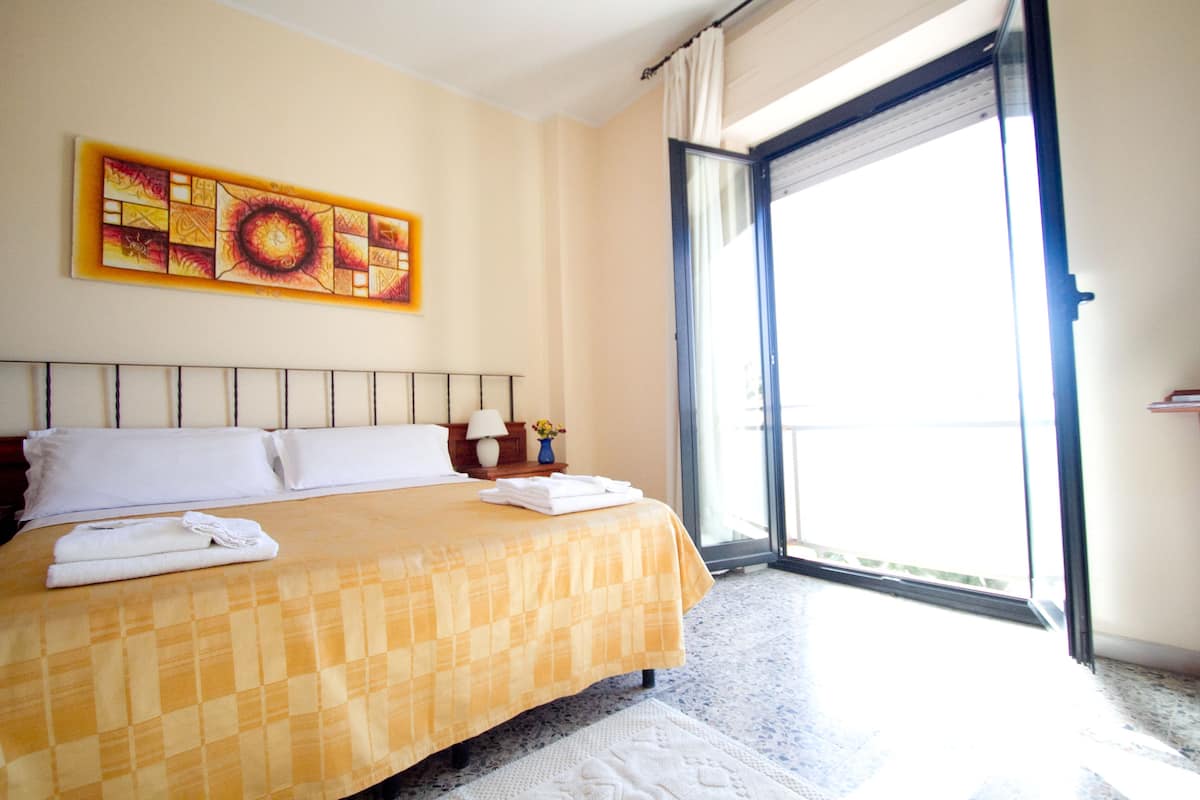 A hotel room with a large bed, a window with a view, and a painting on the wall.