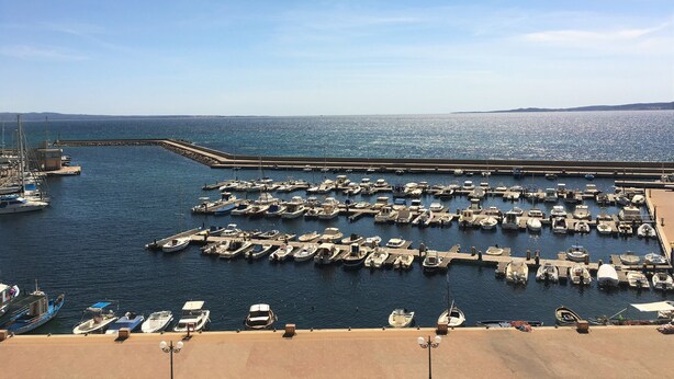 Una marina con numerosos barcos amarrados, cielo despejado y mar en calma.