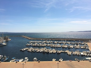 Una marina con numerosos barcos amarrados, cielo despejado y mar en calma.