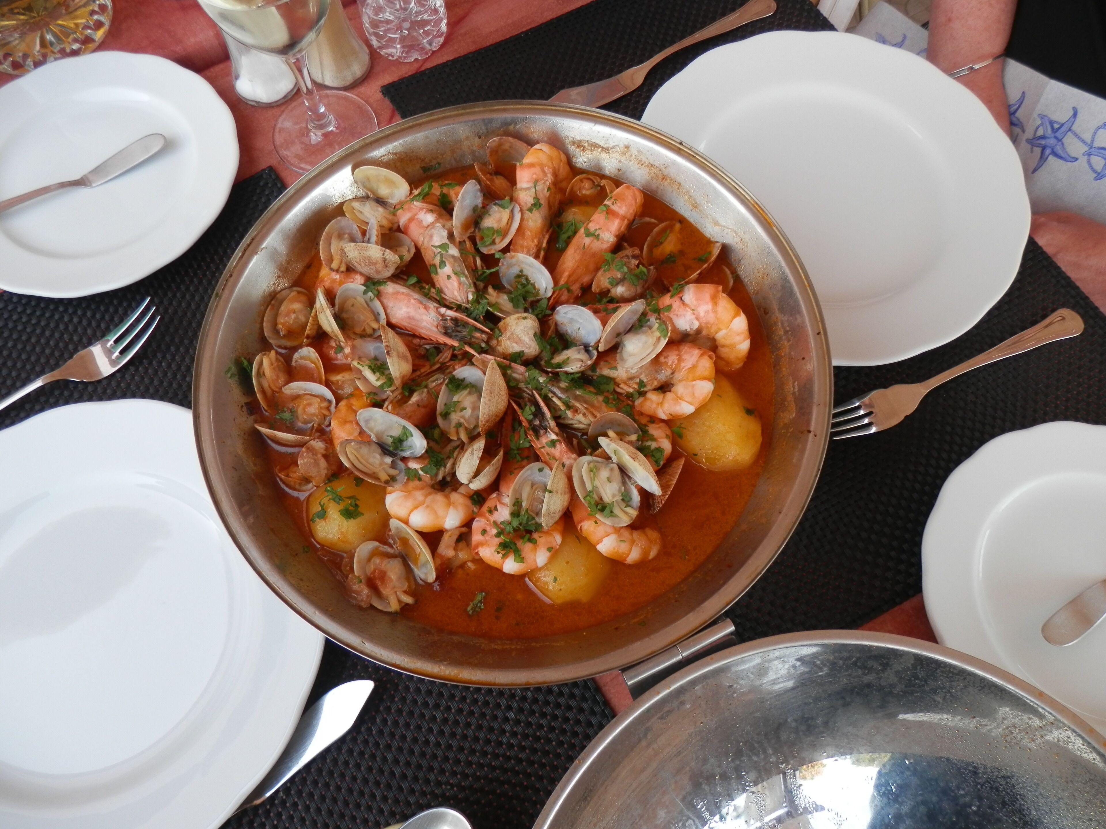 A seafood dish in a metal pan, surrounded by white plates and cutlery on a table.