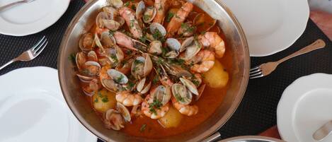 A seafood dish in a metal pan, surrounded by white plates and cutlery on a table.