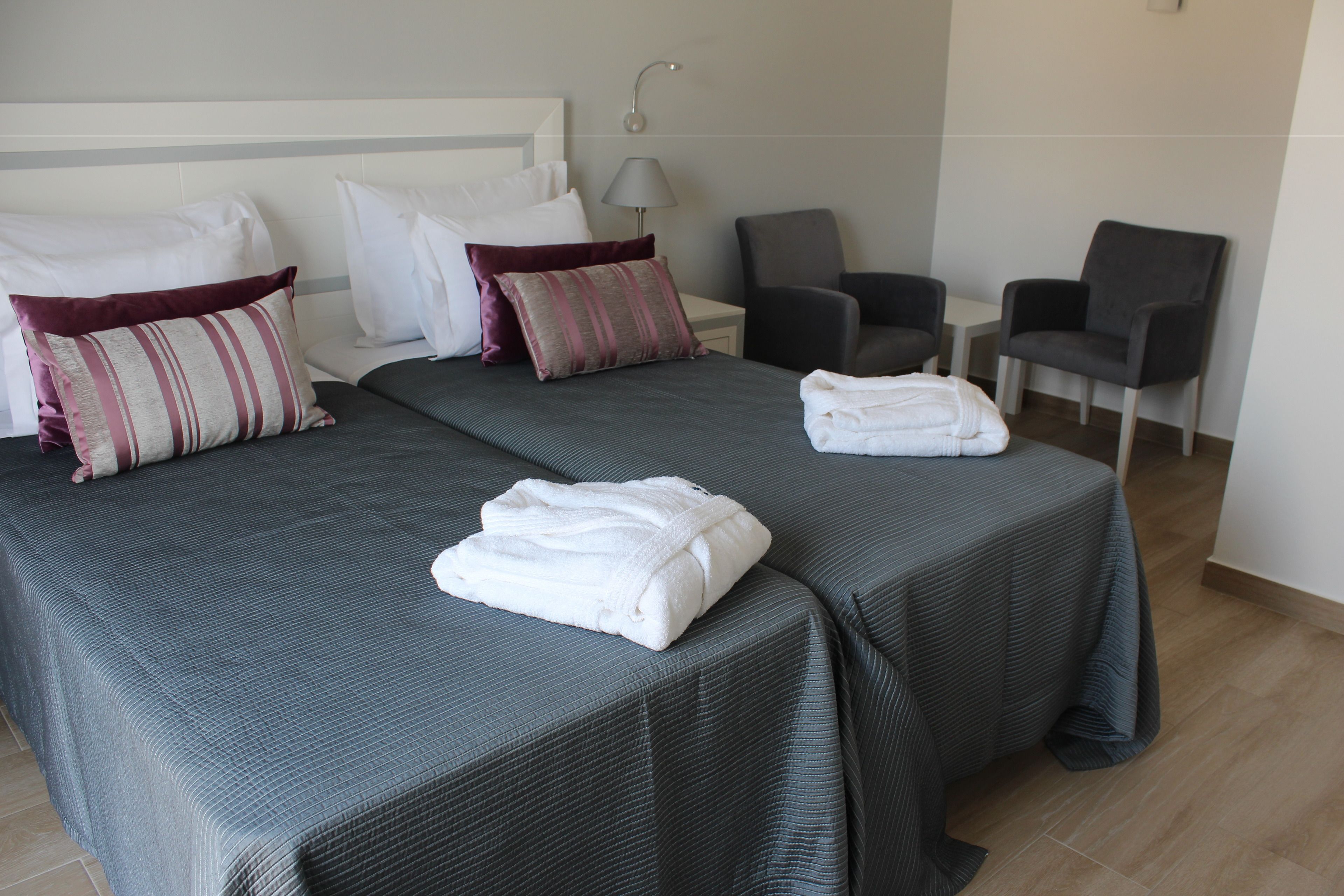 A hotel room with two beds, a nightstand, a lamp, and two chairs.