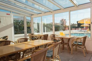 A sunlit patio area with wicker furniture and large windows overlooking a swimming pool.