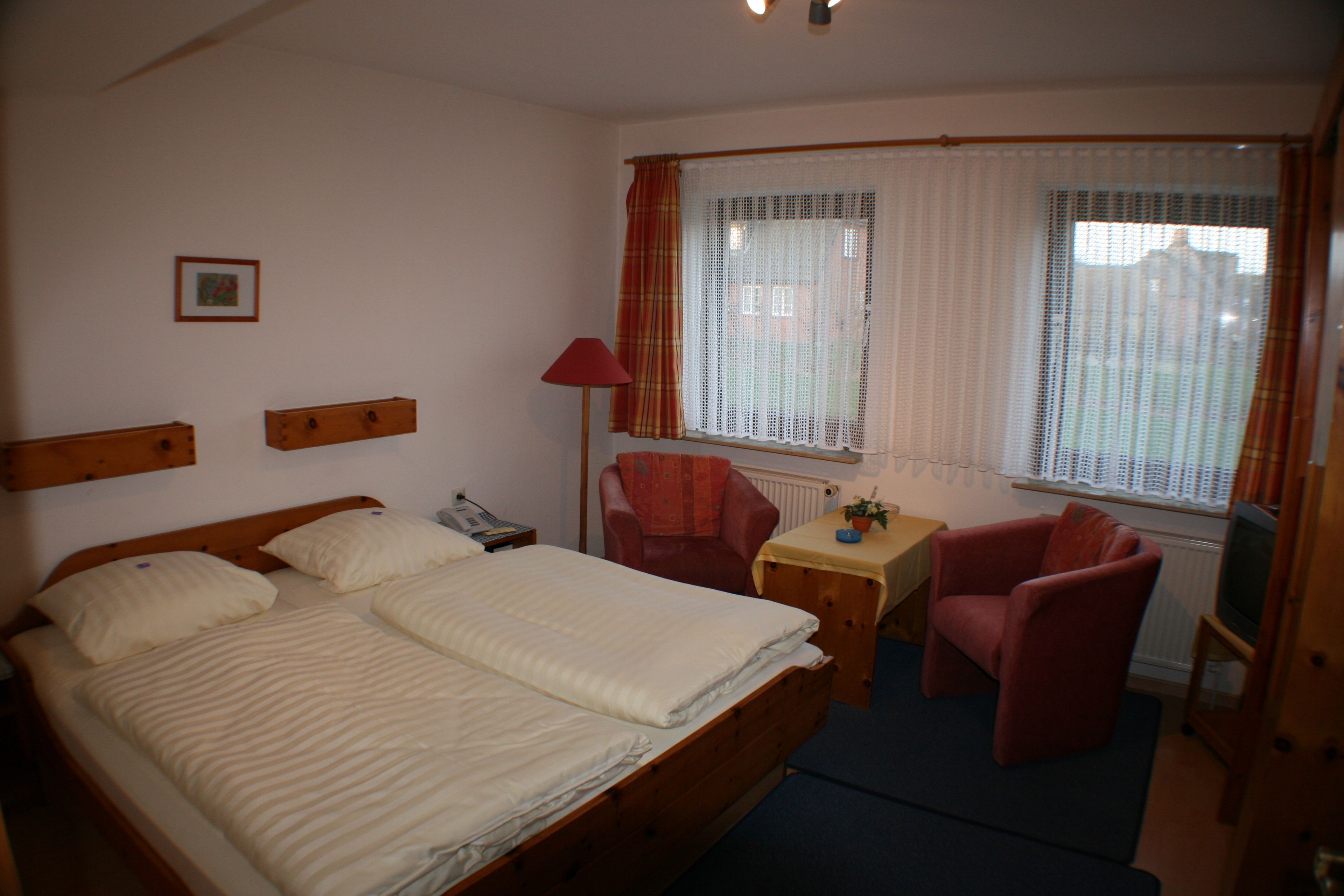 Ein Hotelzimmer mit Doppelbett, Schreibtisch mit Stuhl, Fernseher und einem fenster mit Vorhängen.