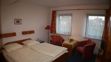 Ein Hotelzimmer mit Doppelbett, Schreibtisch mit Stuhl, Fernseher und einem fenster mit Vorhängen.