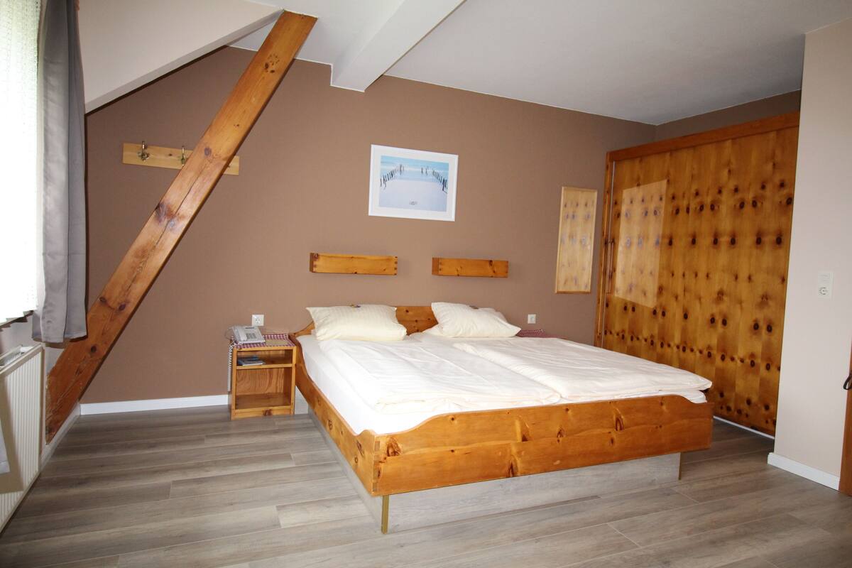 Un dormitorio con una cama de madera, una mesita de noche, cabecera de madera, un armario de madera y un cuadro en la pared.