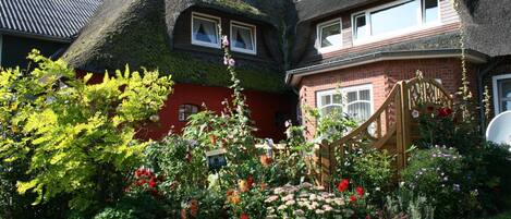 A traditional house with a thatched roof and a well-maintained garden with various flowers and a wooden gate.
