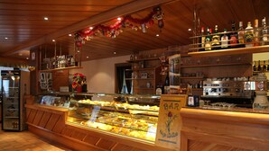 A bakery display case with various baked goods, a bar area with shelves of bottles, and a wooden counter with a sign reading "BAR Nizza". - Nigritella (Selva di Cadore)