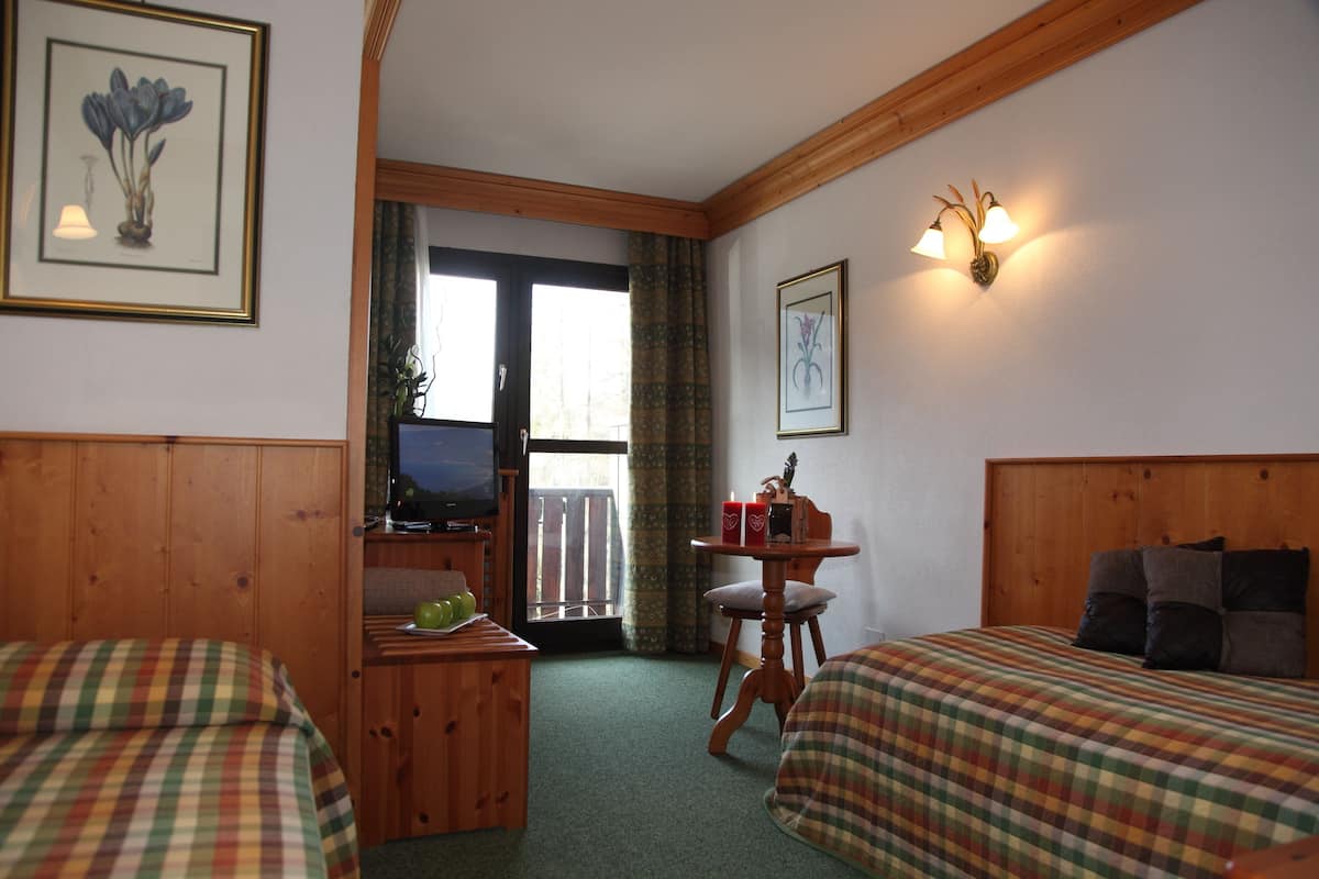 A room with two beds, a wooden desk, a television, and a window with curtains.