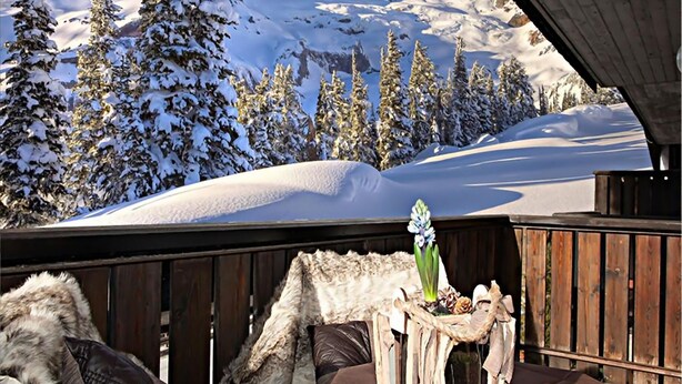 A wooden deck with a rustic table and chairs, overlooking a snowy mountain landscape with evergreen trees. - Nigritella (Selva di Cadore)