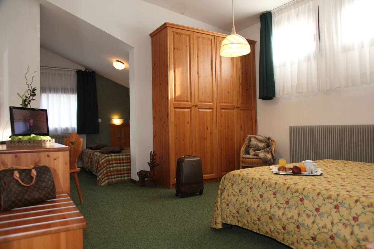 A hotel room with a bed, a wardrobe, a suitcase, a chair, a table with a tray of breakfast, and a television.