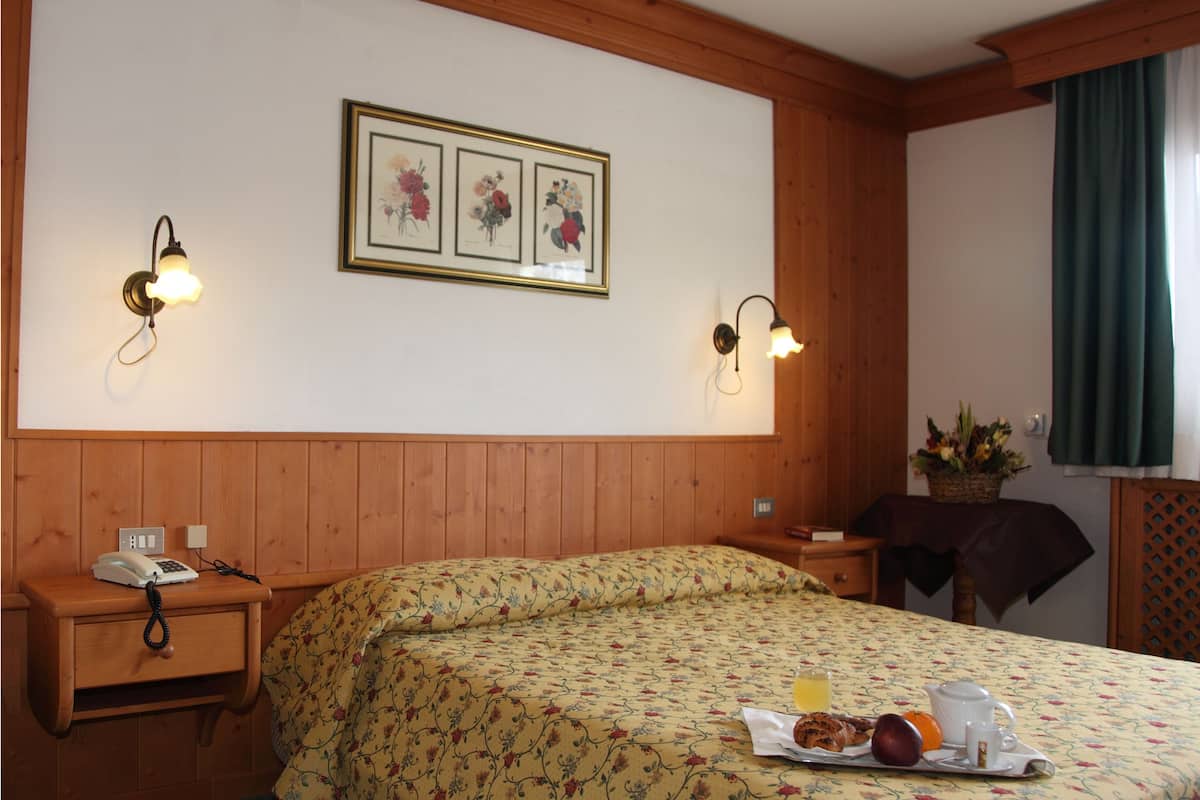 A hotel room with a wooden headboard, floral bedspread, bedside lamps, a telephone, a small table with a basket of flowers, and a breakfast tray on the bed.