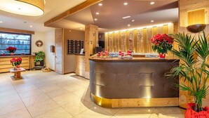 A modern hotel lobby with a central reception desk, wooden accents, and a large window offering a view of the mountains. - Nigritella (Selva di Cadore)