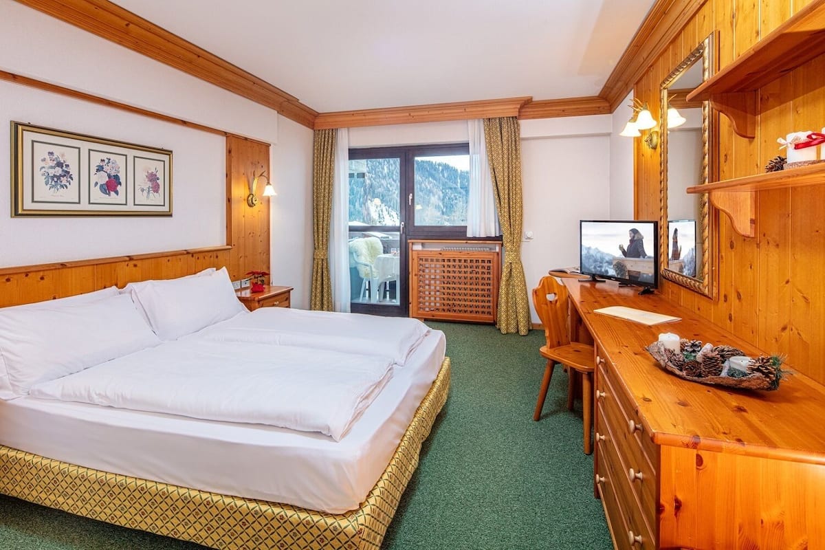 A hotel room with a large bed, a desk with a computer, a mirror, and framed pictures on the wall.
