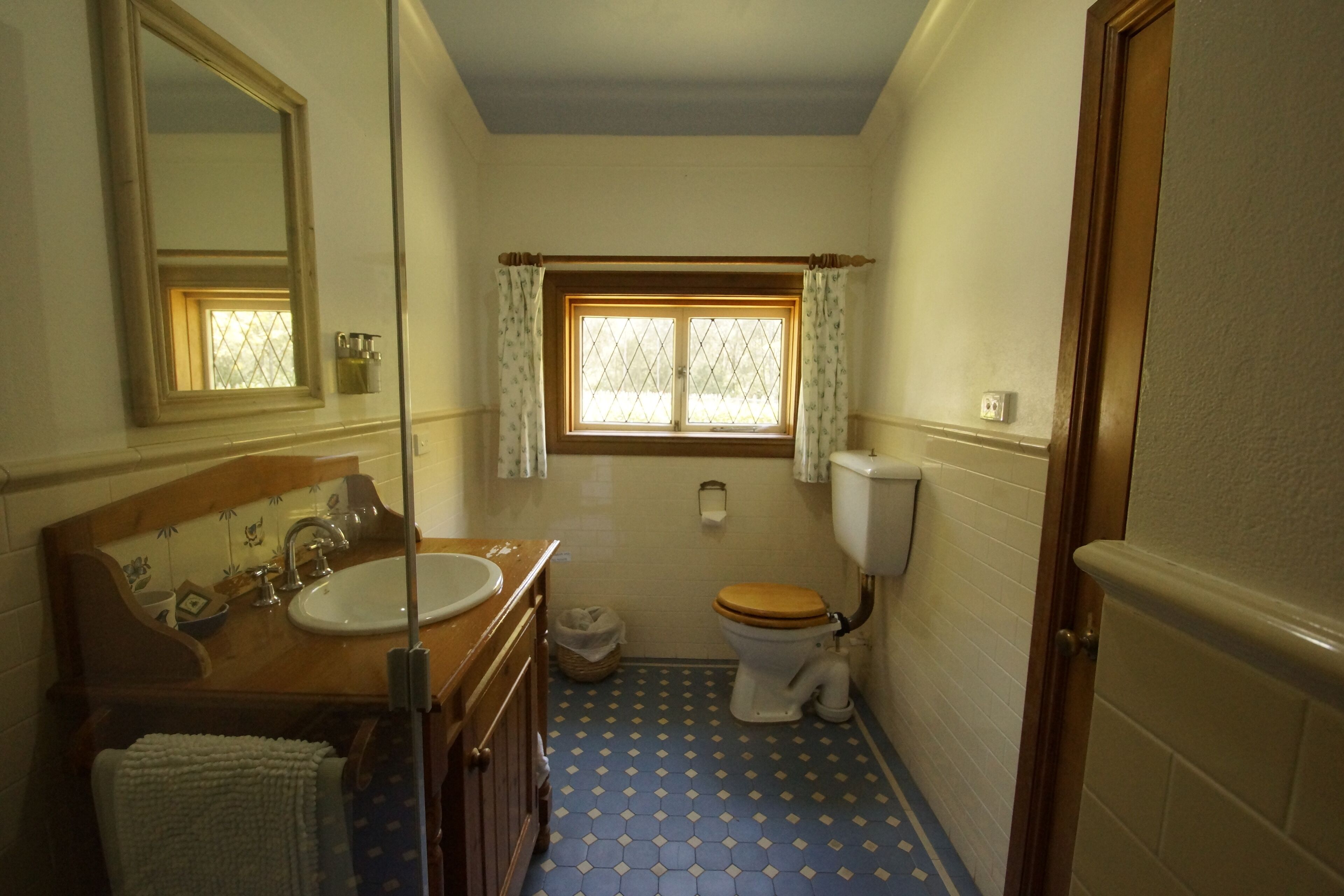 A small bathroom with a wooden vanity, a sink, a toilet, and a window with curtains.