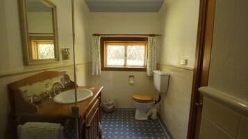 A small bathroom with a wooden vanity, a sink, a toilet, and a window with curtains.