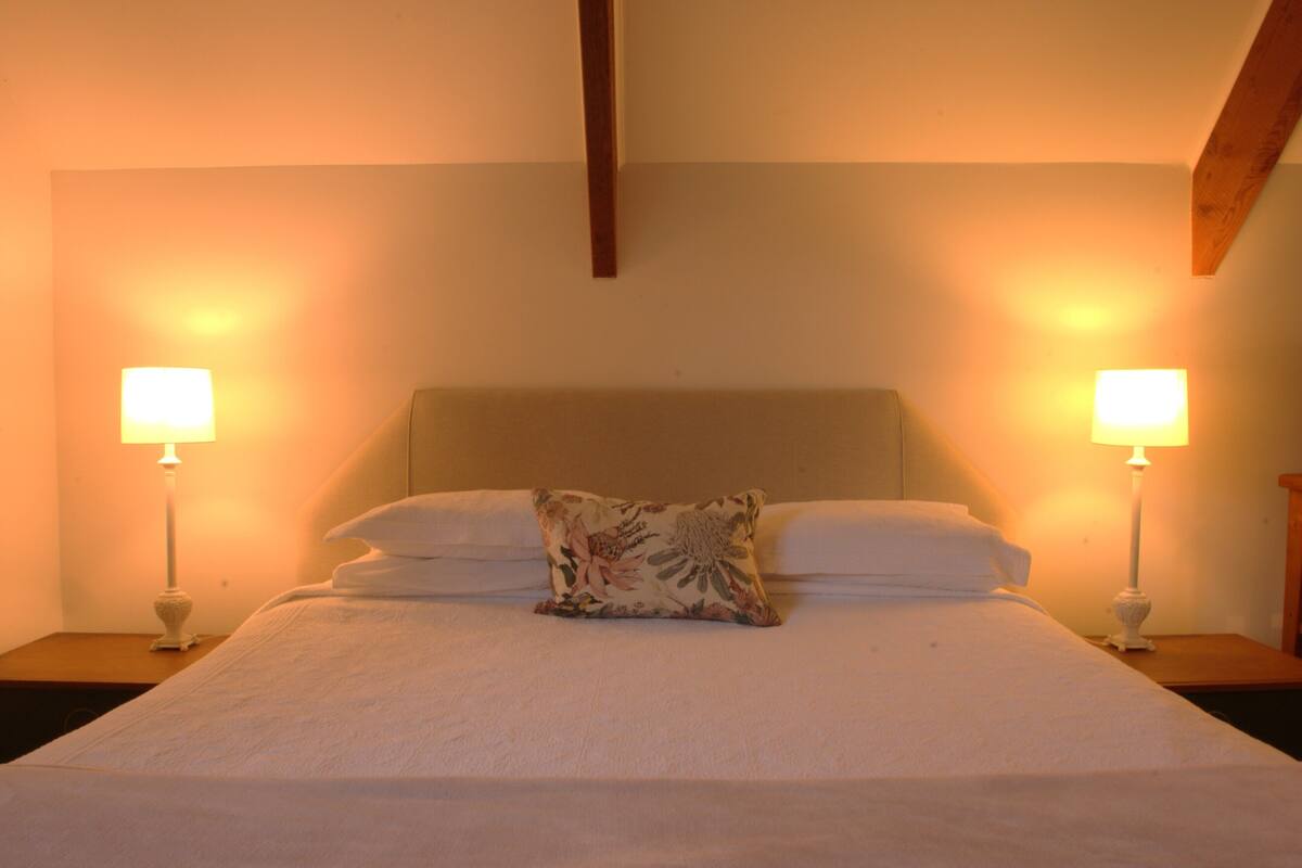 A neatly made bed with a floral pillow, two bedside lamps, and a wooden ceiling beam.