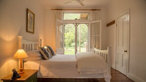 A bedroom with a bed, a nightstand, a lamp, a window with curtains, and a door. - The Carriages (Pokolbin)