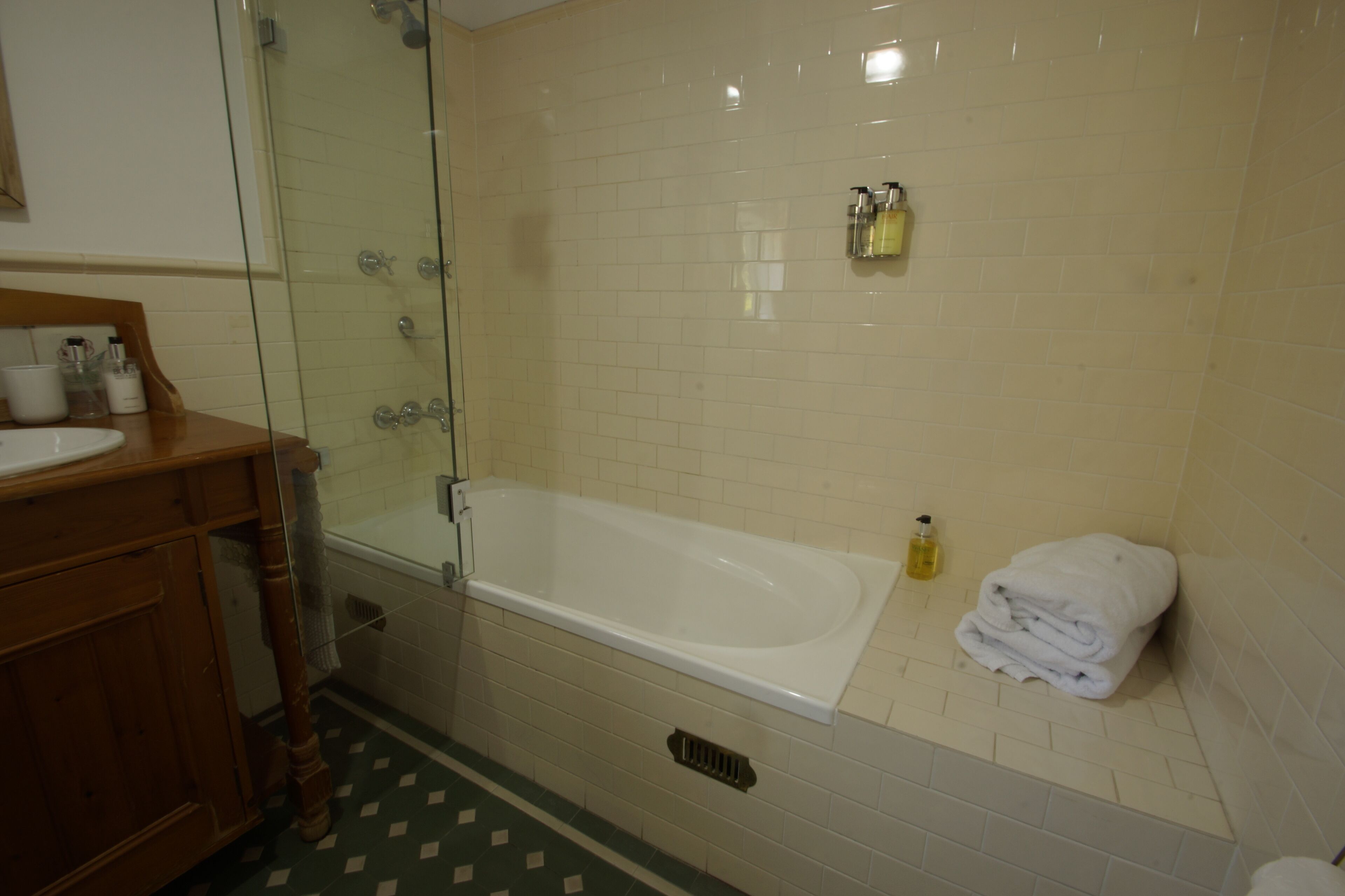 A bathroom with a glass-enclosed shower, a white bathtub, and a wooden vanity with a sink.