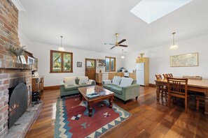 Ampla sala de estar com lareira, dois sofás, uma mesa de centro e uma área de jantar com mesa e cadeiras de madeira.
