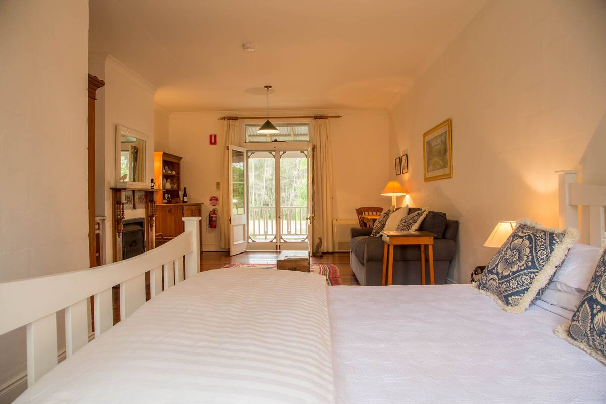 A bedroom with a large bed, a sofa, a small table, and a window with curtains.