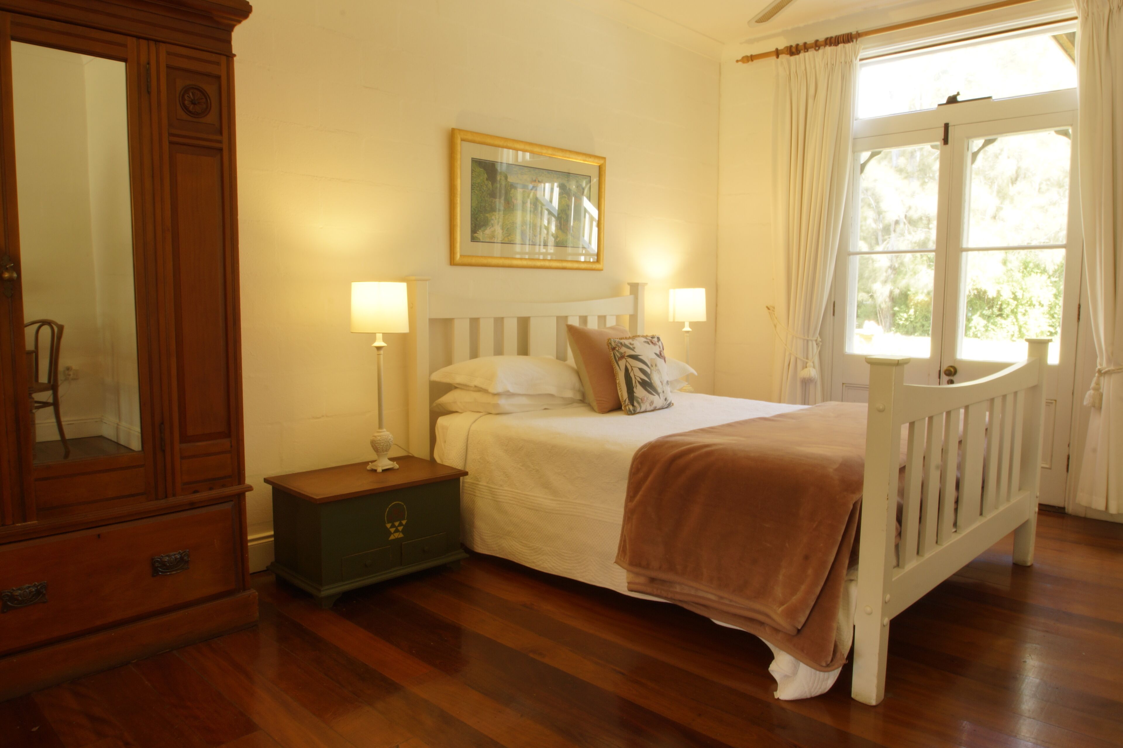 A bedroom with a wooden bed, a nightstand, a dresser, a framed picture on the wall, and a window with curtains.