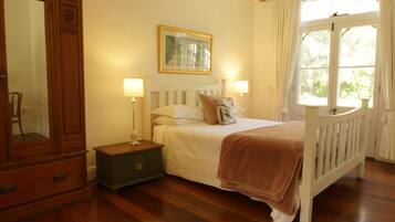 A bedroom with a wooden bed, a nightstand, a dresser, a framed picture on the wall, and a window with curtains.