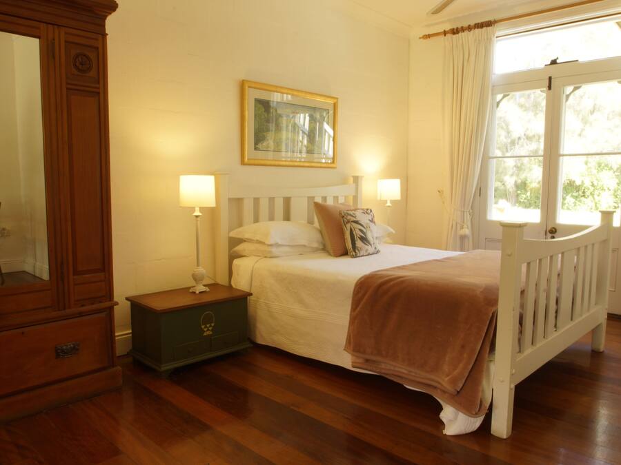 A bedroom with a wooden bed, a nightstand, a dresser, a framed picture on the wall, and a window with curtains.