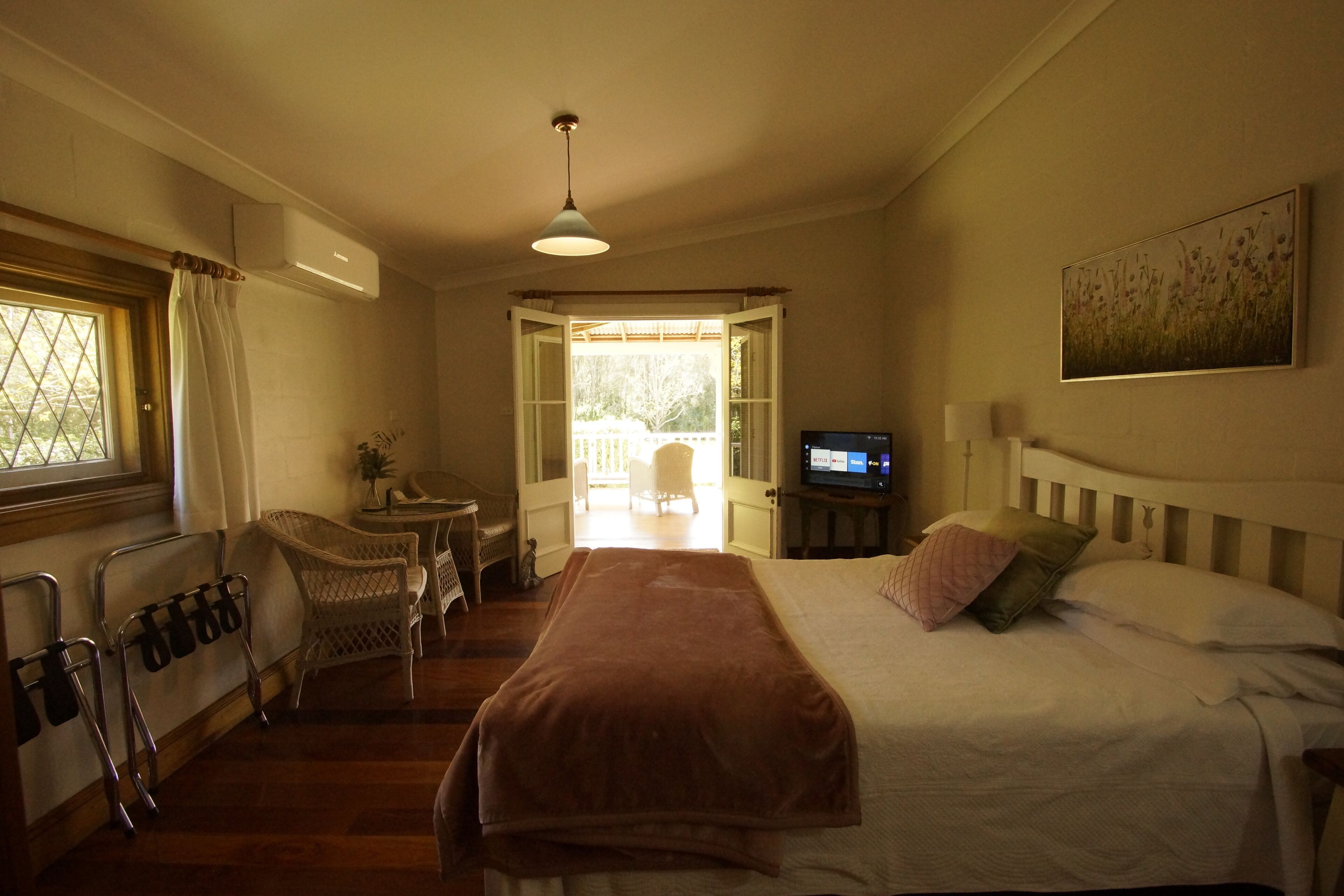 A bedroom with a bed, a television, a window with curtains, a chair, and a view of the outdoors.