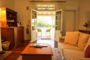 Una puerta abierta que da a un balcón con una mesa y sillas, un armario de madera con vajilla, y un sofá en la sala de estar.