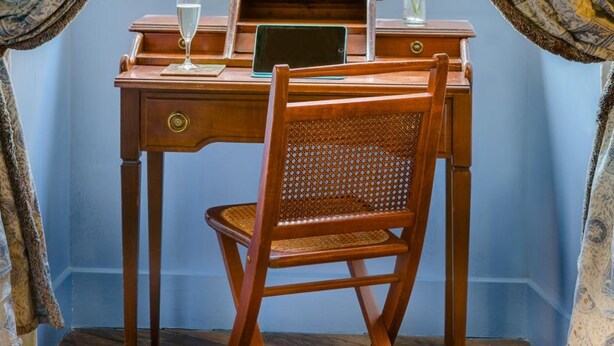 Un bureau en bois avec un ordinateur portable, un verre d’eau et un vase rempli de fleurs.