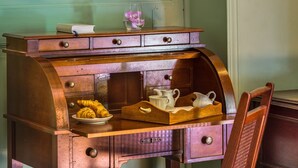 Un bureau en bois avec des tiroirs, une chaise, un tableau floral encadré et une lampe fixée au mur.