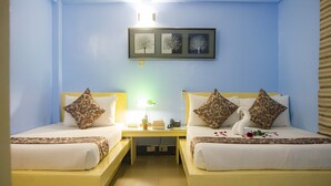 A hotel room with two beds, each with patterned pillows and a swan decoration. A nightstand with a lamp and books is between the beds. - Franchise One Hotel (Makati)