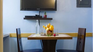 A dining area with a table, two chairs, a television mounted on the wall, and a small shelf with a plant and a bottle. - Franchise One Hotel (Makati)