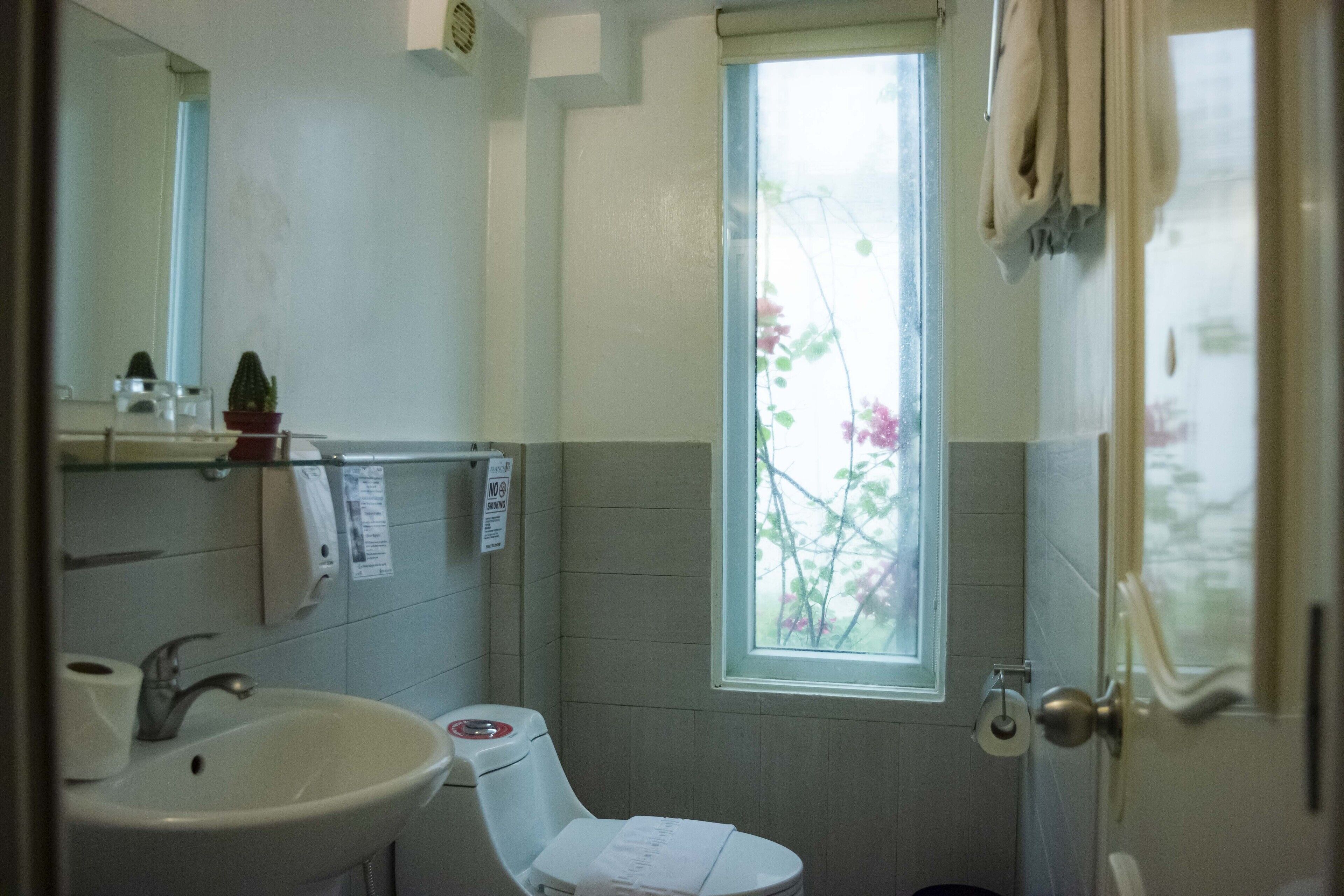 Un baño con lavamanos, inodoro y ventana con vistas a flores rosadas.