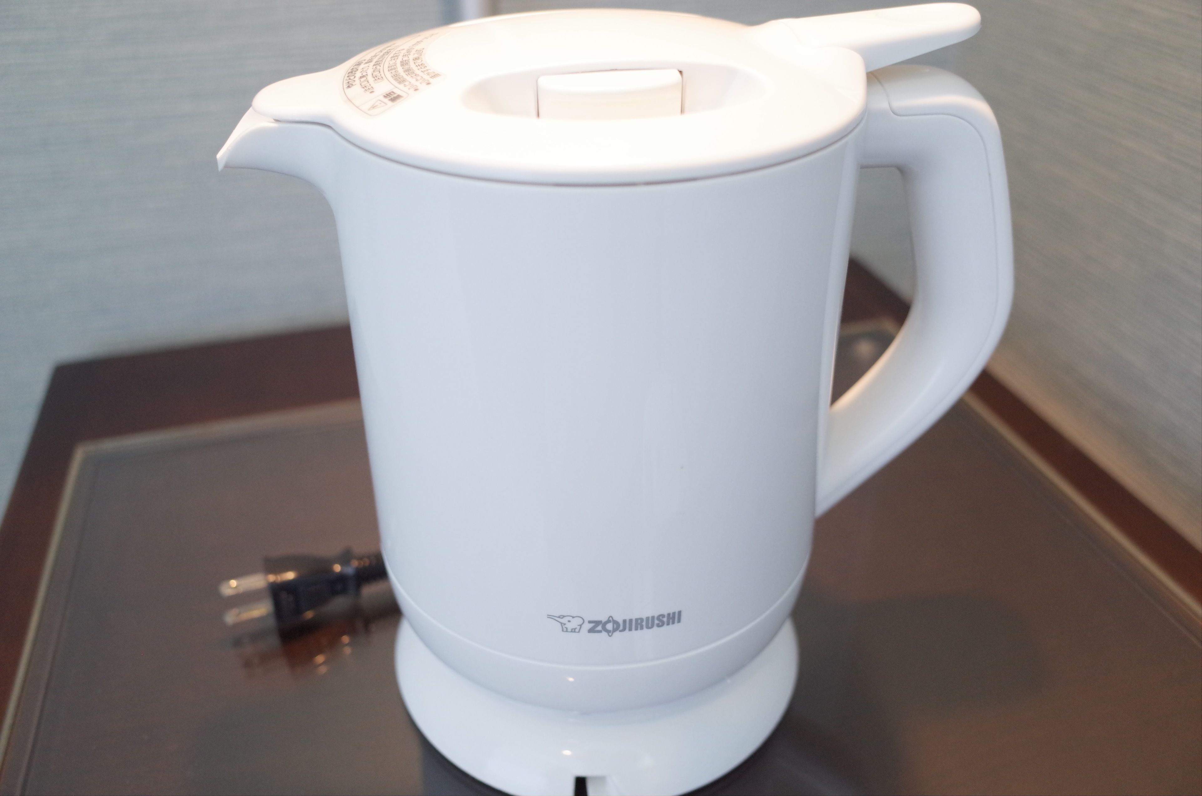 A white electric kettle with a handle and a spout, placed on a metallic surface.